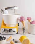 Ice cream maker in a yellow blender next to ice cream and fruit displayed on a kitchen countertop