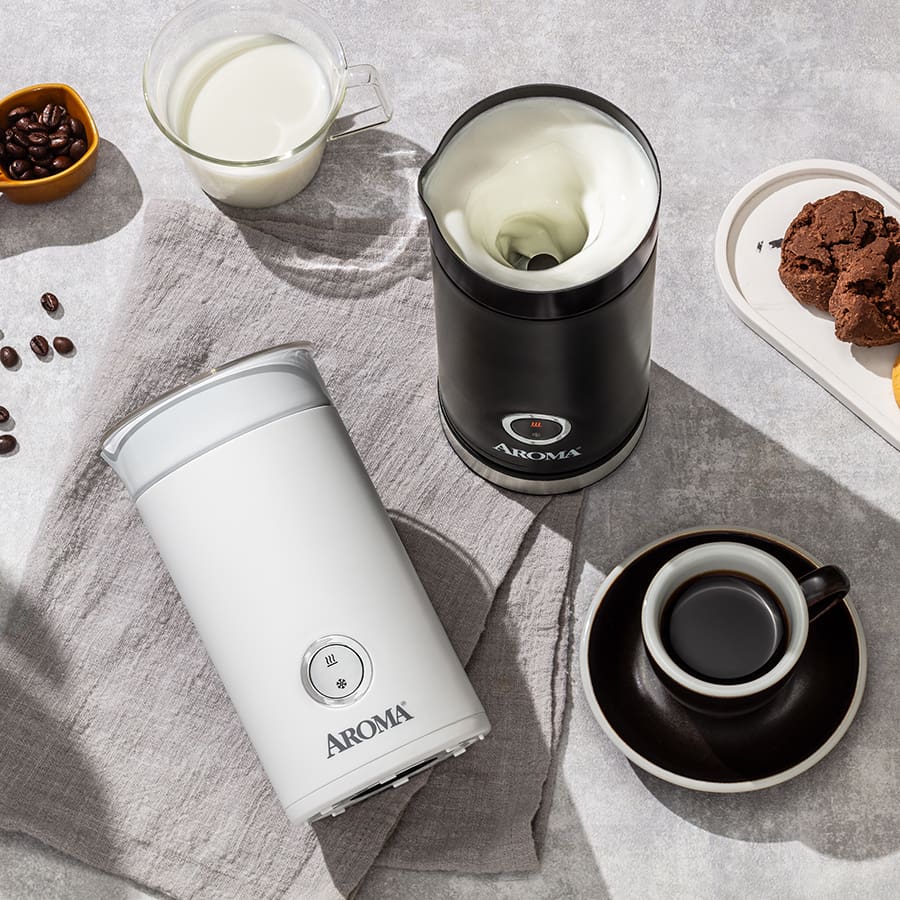 Two Aroma milk frothers on a table with coffee beans, milk, and cookies.