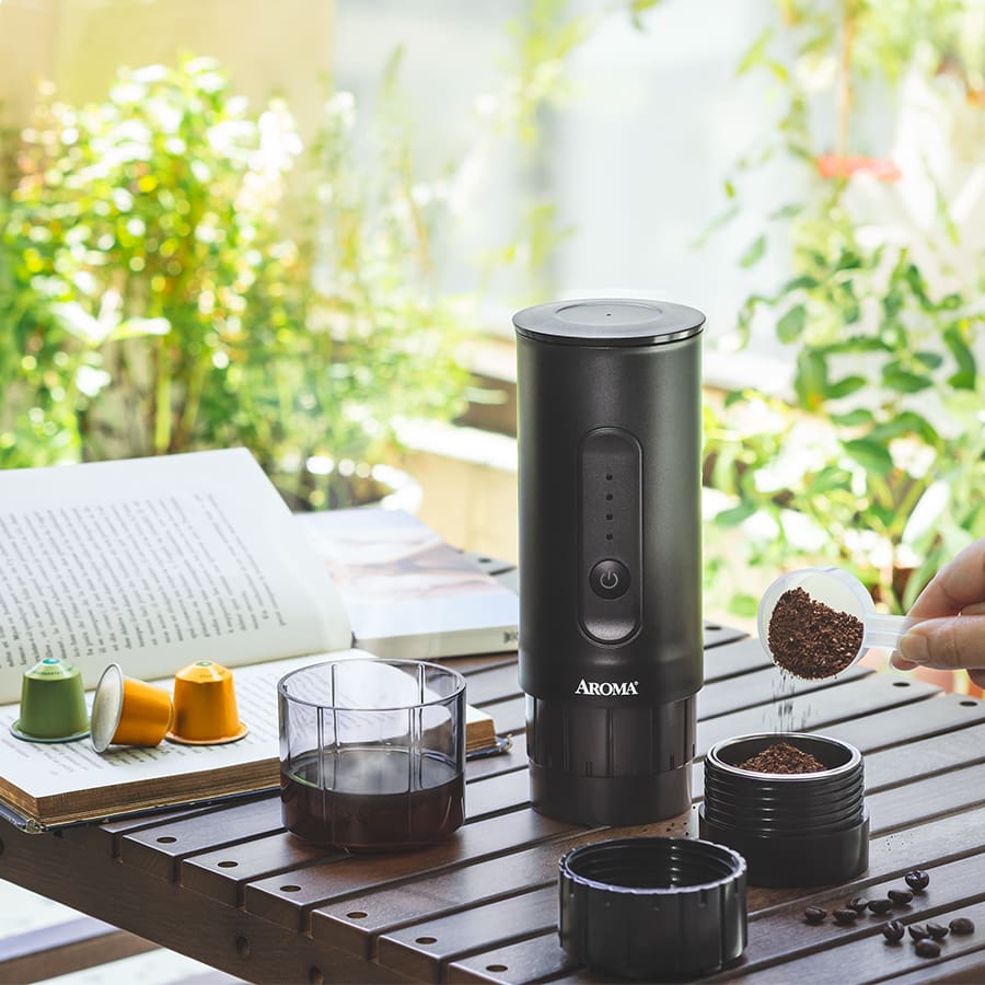 Black coffee grinder with coffee beans on a wooden table outdoors