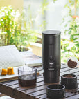 Black coffee grinder with coffee beans on a wooden table outdoors