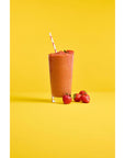Fruit smoothie in a glass cup with a straw and strawberries on a yellow and white background