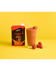 Fruit smoothie in a glass cup with straw and strawberries next to Davinci Strawberry Bomb Smoothie Mix on a yellow and white background
