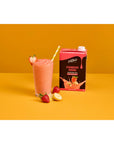 Glass cup of a fruit smoothie with strawberries and bananas next to Davinci Strawberry Banana smoothie mix on an orange and white background