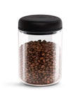 Clear jar with black lid filled with coffee beans on a white background