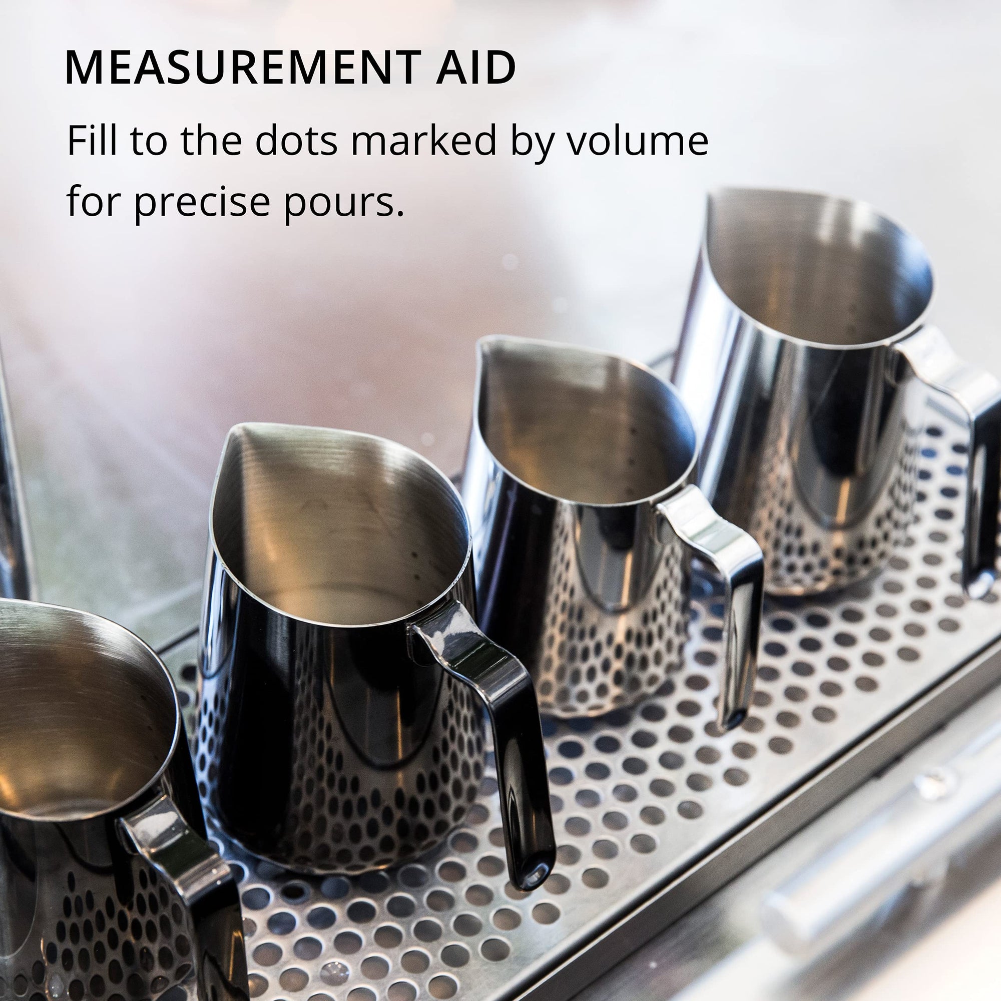 Metal milk steaming pitchers on a metallic surface with text about measurement aid