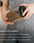 Person holding a container of coffee beans with text about maintaining freshness.