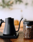 Black coffee kettle and jar of coffee beans on a wooden surface with a blurred background