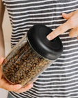 Person holding a jar of coffee beans with a black lid