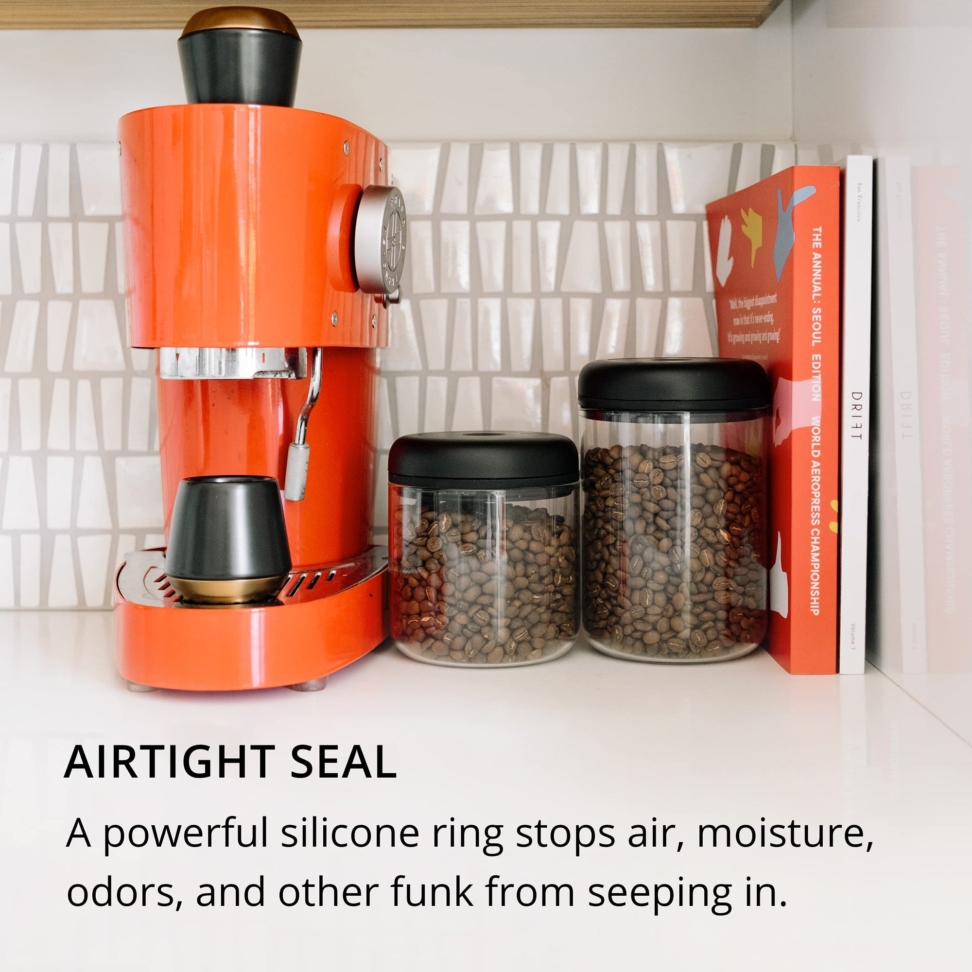 Orange coffee machine with airtight storage containers and books on a kitchen counter with text about containers' airtight seal.