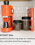 Orange coffee machine with airtight storage containers and books on a kitchen counter with text about containers' airtight seal.