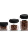 Three glass jars with black lids, each containing coffee beans, on a white background.