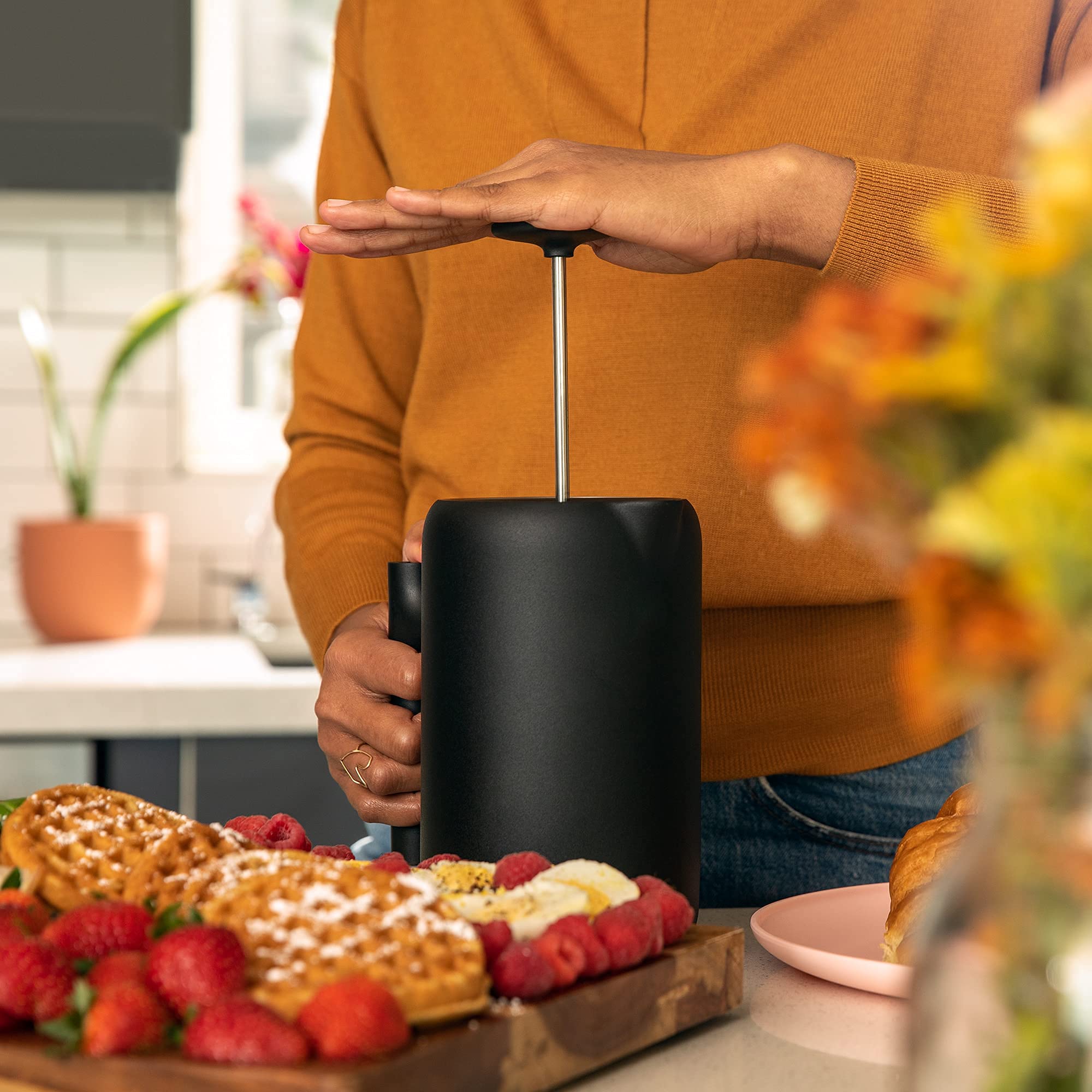 Person using a french press with a breakfast setup including waffles and berries.