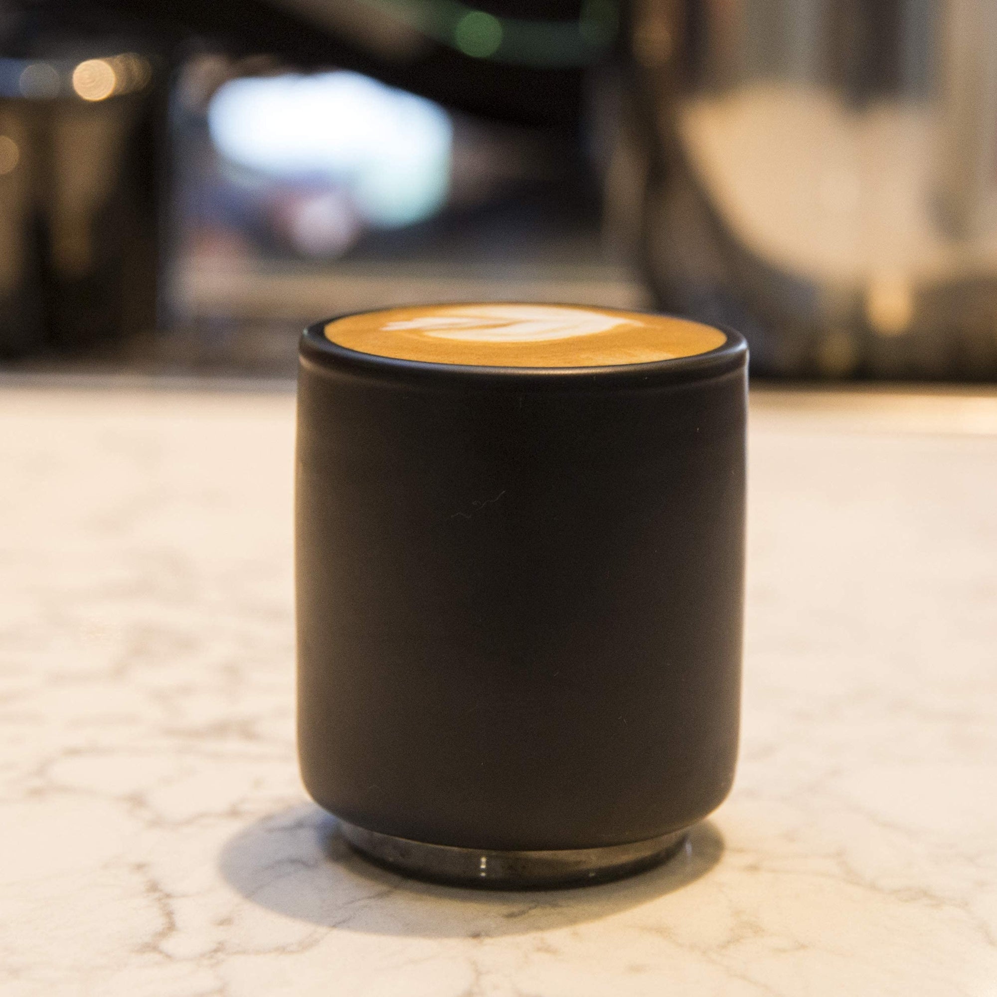Black ceramic cup with a cappuccino on a marble surface