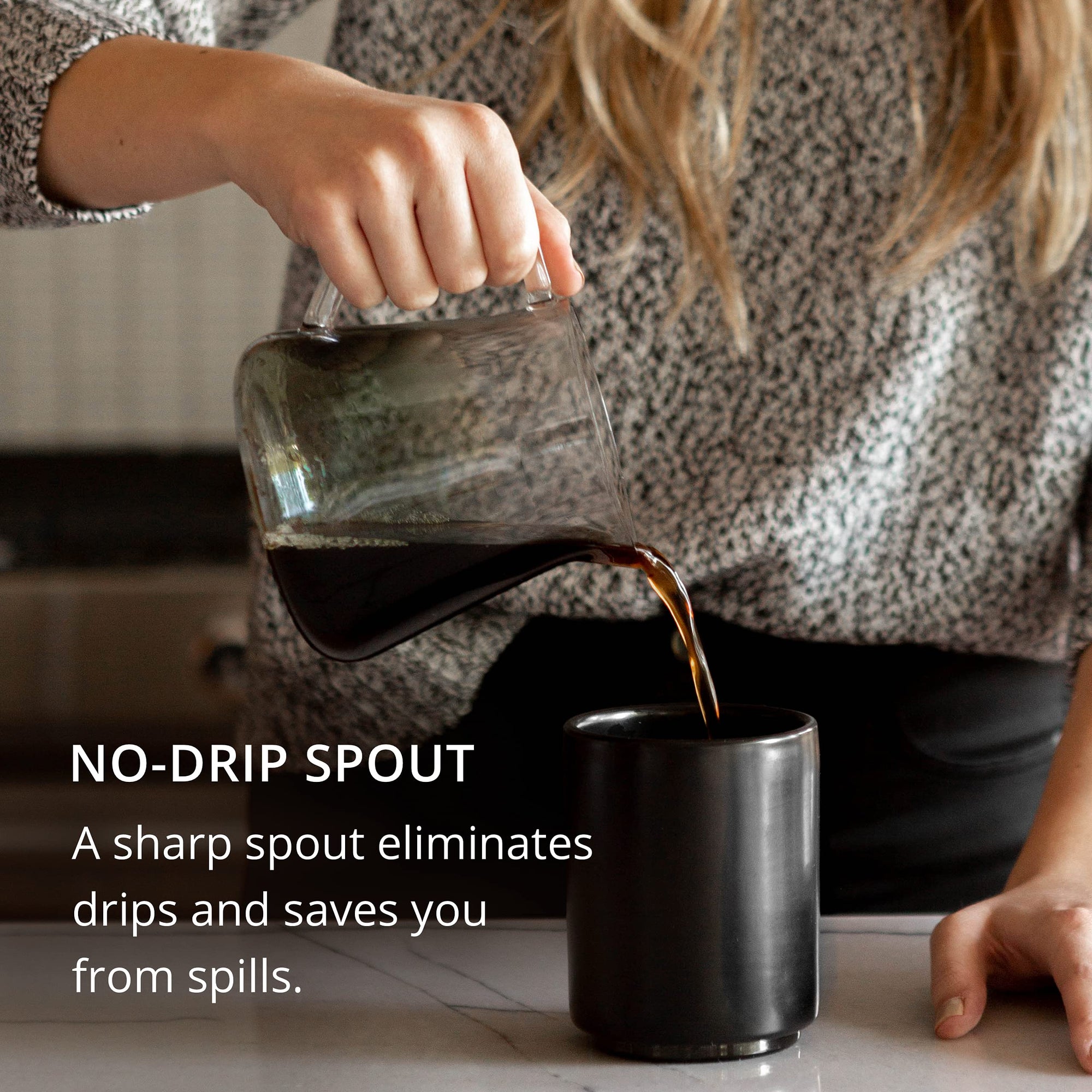 Person pouring coffee from a glass carafe into a black mug with text 'NO-DRIP SPOUT' on a blurred background.