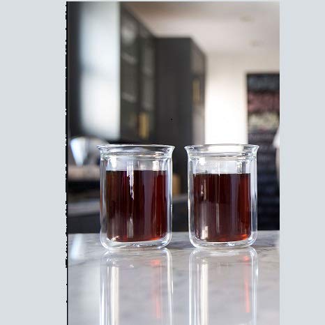 Two clear glass cups filled with a dark liquid on a reflective surface.
