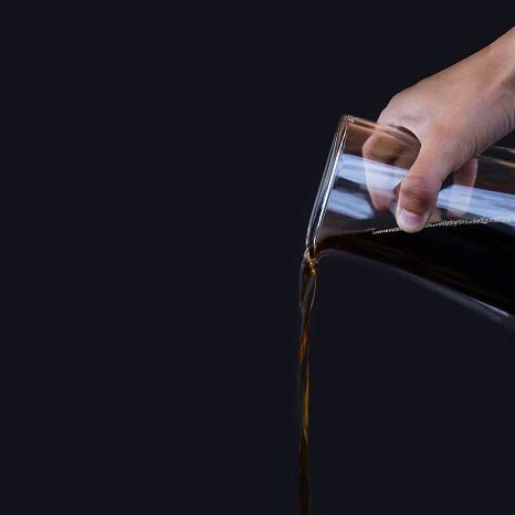 Hand pouring a dark liquid from a container onto a black surface with a dark background