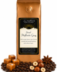 1 lb J.L. Hufford Decaf Highlander Grogg coffee bag with coffee beans, blocks of caramel, hazelnuts, and spice on a white background