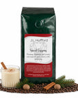 1 lb J.L. Hufford Spiced Eggnog coffee bag with coffee beans, glass of eggnog, pine needles, and cinnamon sticks on a white background