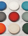 Nine different color Le Creuset enameled cast iron signature trivet on a marble background