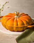 Orange cast iron signature pumpkin braiser on a wooden table with a green napkin and decorative elements.