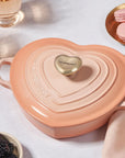 Peche heart shaped 1.25 qt cocotte with handles and a light gold heart knob next to macaroons, golden forks, blackberries, rose gold glasses, and a rose colored napkin on a white tablecloth