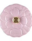 Pink enameled cast iron casserole dish with floral lid design on a white background