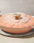 Peche ceramic casserole dish with a lid on a light surface with flowers in the background