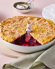Pie with a slice cut out, placed in a white dish on a table with a green napkin and gold utensils.
