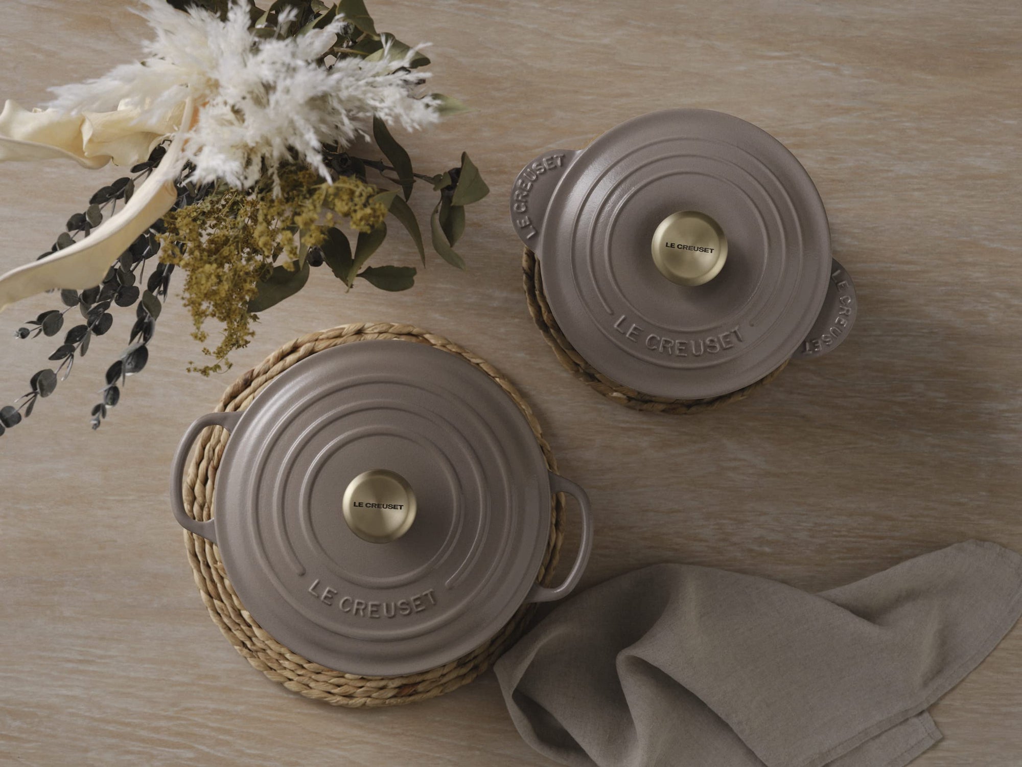 Two gray Le Creuset pots with gold knobs on a wooden surface with decorative elements.