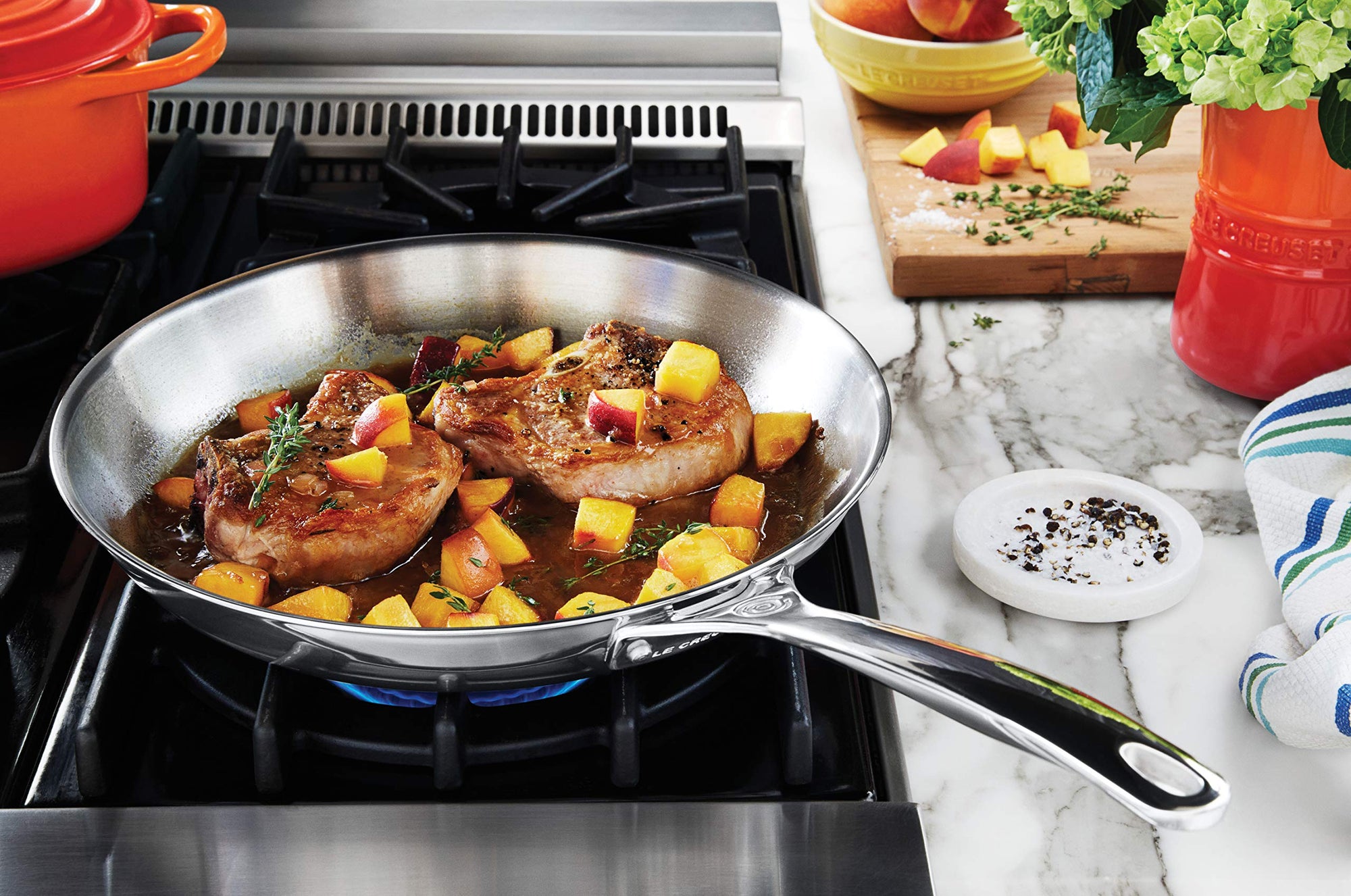 Sliced peaches and pork chops cooking in a skillet on a stovetop with a kitchen setting.