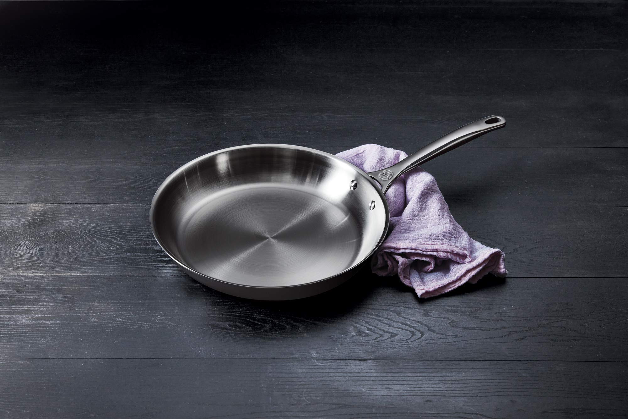 Stainless steel frying pan on a dark wooden surface with a purple cloth