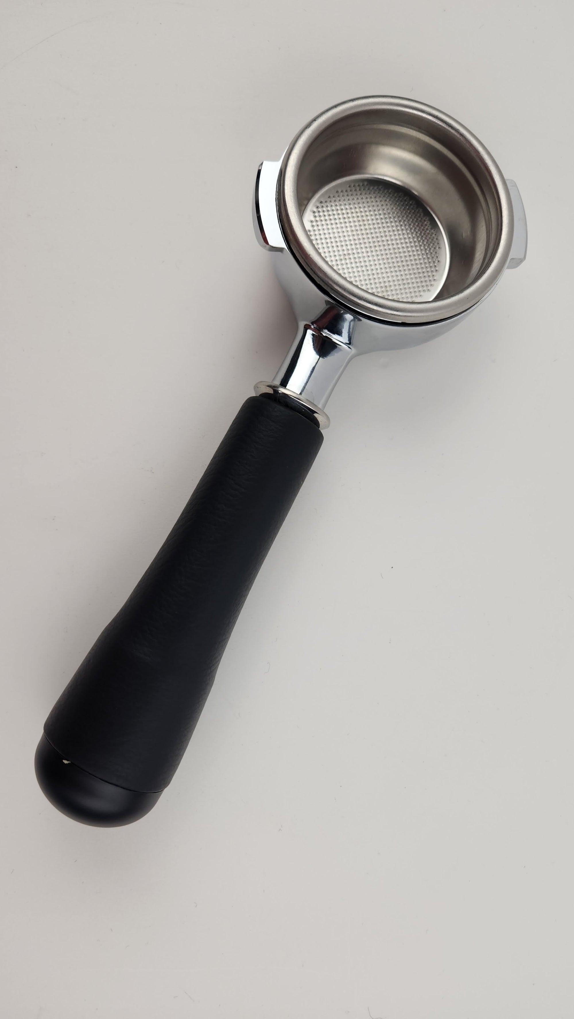 Coffee portafilter with black handle and metal basket on a light gray background