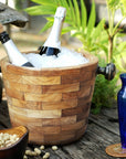 Rico & Plato angelia teak wine champagne ice bucket with ice and wine bottles inside next to two blue vases and bowl of peanuts on a wooden surface outside