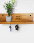 Rico & Plato lucky wooden key hanger displayed on a wall with keys hanging from it and a plant sitting on the ledge of it