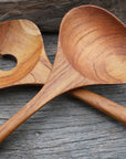 Close up of two teak salad serving utensils crisscrossed each other on a wooden surface
