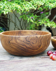 Large teak bowl next to a smaller teak bowl and grapes placed on a wooden surface with a nature background