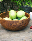 Large teak bowl with fruit inside on a wooden surface with a nature background