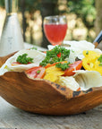 Teak salad fruit bowl with veggies and fruit inside the bowl with drinks in the background on a wooden surface