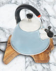 A teak wood trivet with curved steel handles, with a blue and white kettle on top of it, placed on a marble surface.