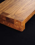 Close up of corner of Rico & Plato wasabi teak serving platter displayed on a black surface