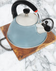 A teak wood trivet with curved steel handles, with a blue and white kettle on top of it, placed on a marble surface.