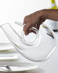Someone tilting a Riedel curly handmade decanter in a dinning room setting