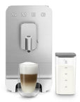 White, silver Smeg fully automatic coffee machine with auto froth next to a creamy coffee and a milk container on a white background