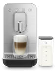 Black, silver Smeg fully automatic coffee machine with milk in a container to the side and with a creamy coffee on a white background