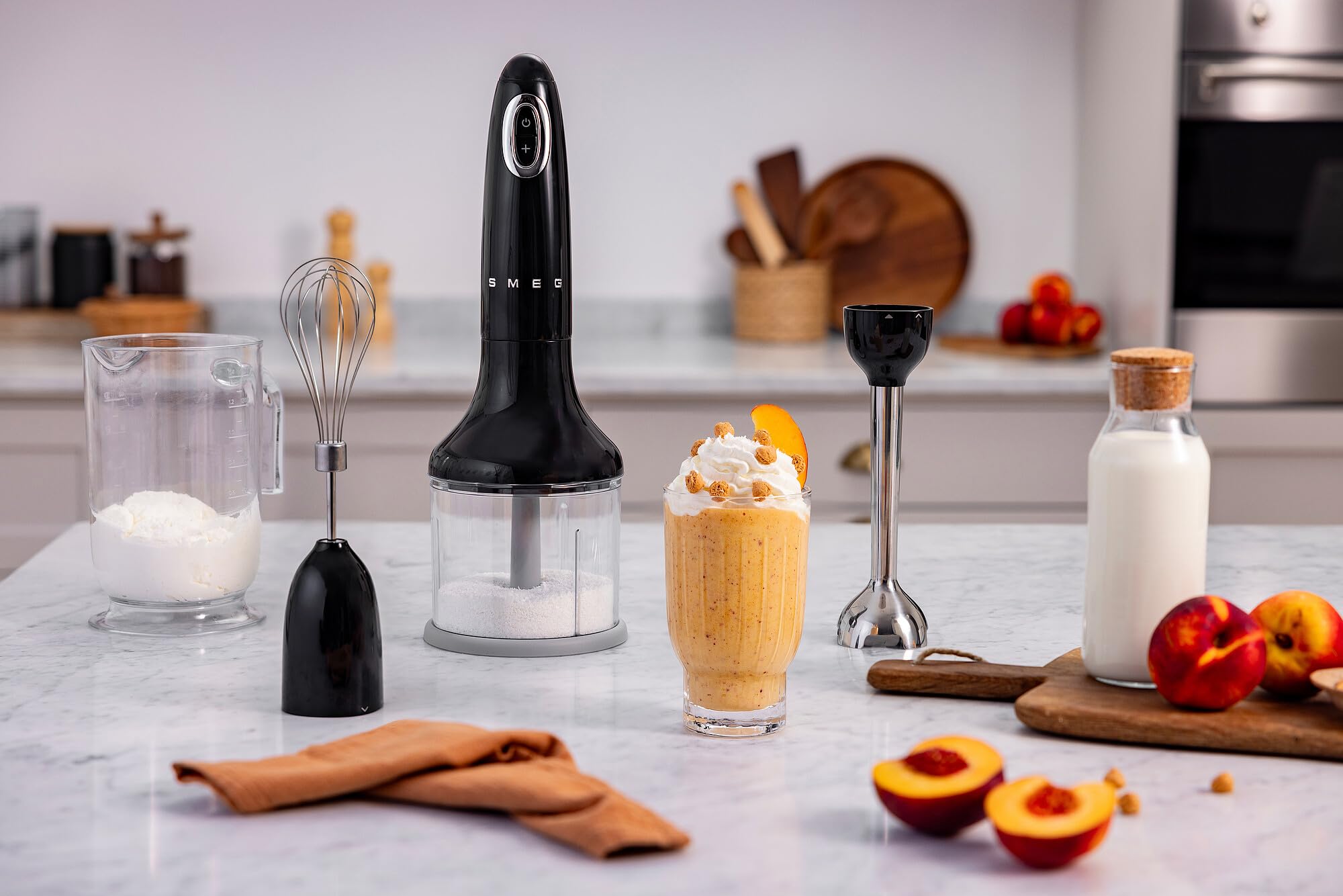 Black hand blender on a kitchen counter with ingredients and a smoothie.