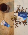 Coffee beans, a cup of coffee, and packets on a wooden and white surface.