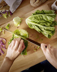 Person cutting lettuce on a wooden cutting board with various ingredients around.
