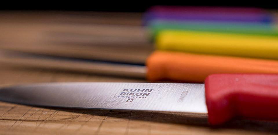 Red, orange, yellow, green, blue, and pink Kuhn Rikon 4" paring knives laying sideways.