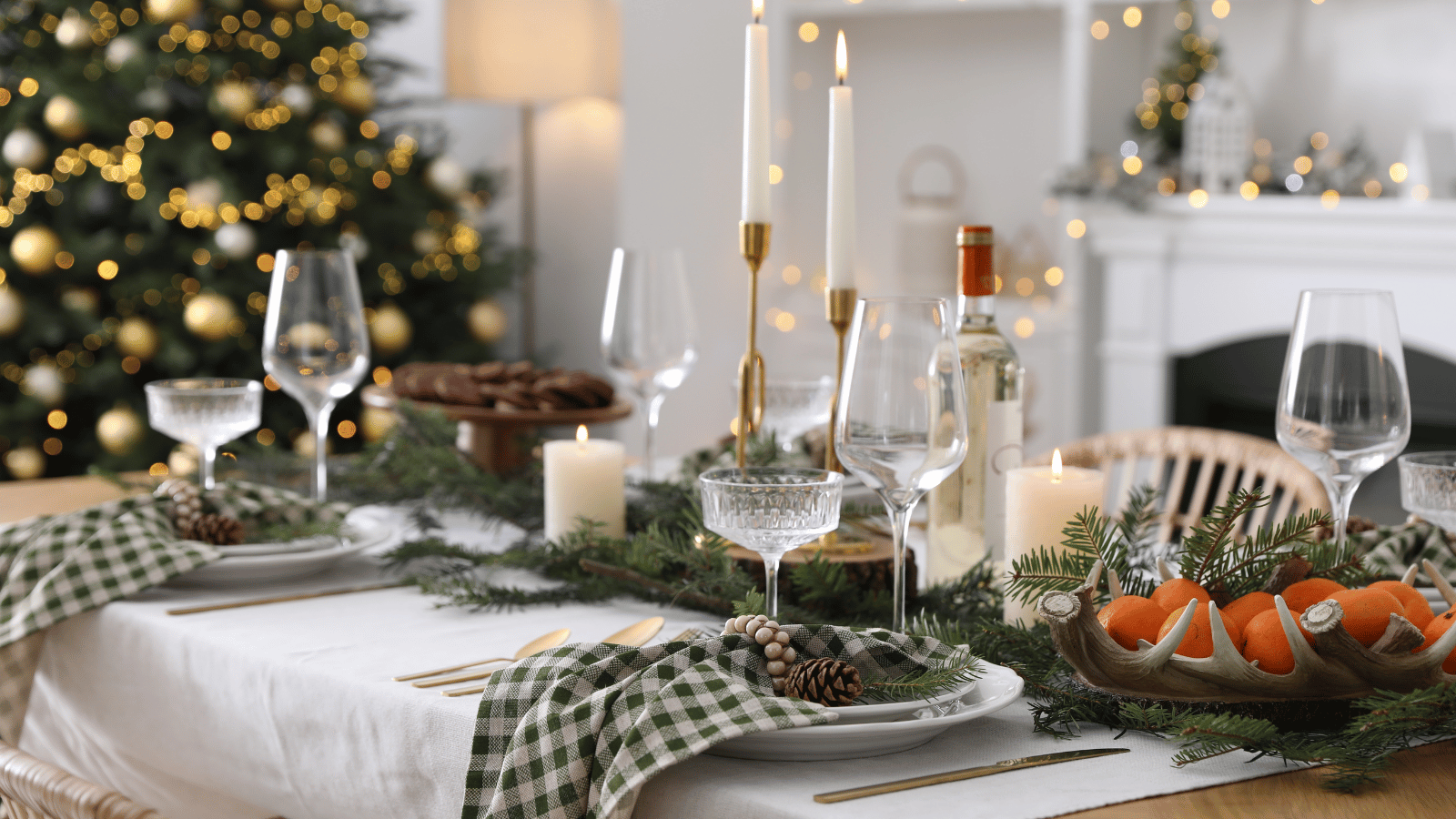 Decorative Christmas table setting with candles, glasses, and a tree in the background.