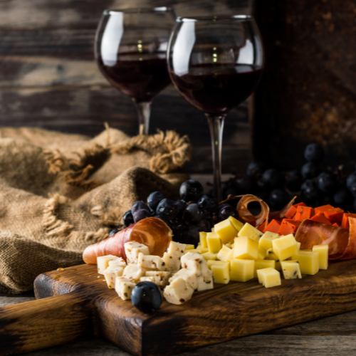 Charcuterie board with cheese, meat, fruit, and two glasses of red wine on a wooden background